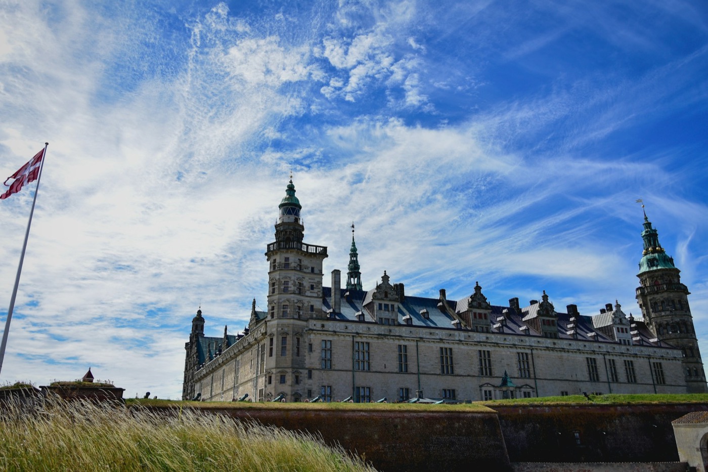 Kronborg Castle under a blue sky, with the Danish flag flying beside it