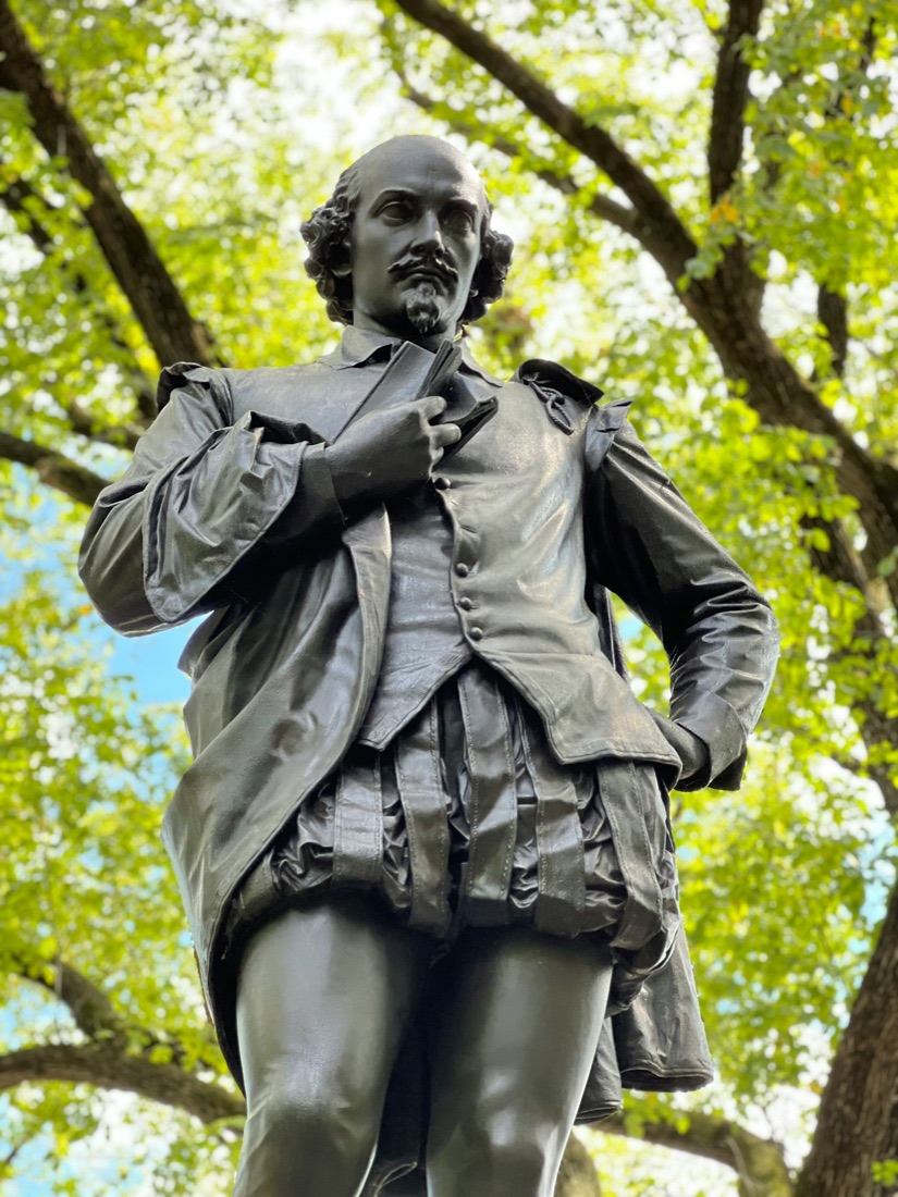 A bronze statue of William Shakespeare, quill and page in hand